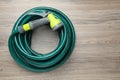 Green rubber watering hose with nozzle on wooden surface, top view Royalty Free Stock Photo