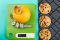 Green scales with a pumpkin and a twisted centimeter against three cookies on a black wicker napkin. Royalty Free Stock Photo