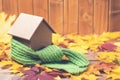 Green scarf around a miniature house on autumn leaves background. Concept of protecting or isolating house. Royalty Free Stock Photo