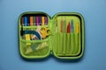 Green school pencil case. Colored different school supplies in case on blue background. Back to school concept. Flat lay Royalty Free Stock Photo