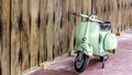 Green scooter against old house. wood wall mossy surface of building as background.