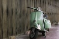 Green scooter against old house. wood wall mossy surface of building as background.