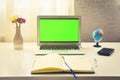 Green screen laptop computer sitting on a home work desk next to notebook, spring flowers and world globe stand.