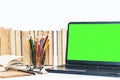 Green screen laptop, pile if books, notebook, smartphone, glasses and pencils in holder on white table, education concept