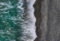 Green sea waves break on black sand and pebbles shore, aerial texture