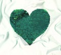 Green sequins heart shape embroidered on white textile wavy folds background. Valentines day luxury and glamour greeting card
