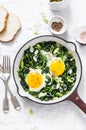Green shakshuka. Fried eggs with fresh spinach, ramson, leek in a cast iron skillet on a white background
