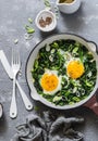 Green shakshuka. Fried eggs with fresh spinach, ramson, leek in a pan on a gray background