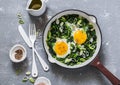 Green shakshuka. Fried eggs with fresh spinach, ramson, leek in a pan on a gray background