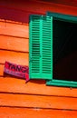 Green shuttered window with orange walls is backdrop for Tango lesson sign in La Boca