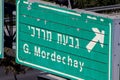 A green sign with the name of the neighborhood written on it in Hebrew and English