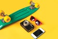 Green skateboard, red sunglasses, vintage camera and screen smartphone on a yellow background Royalty Free Stock Photo