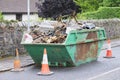 Green skip and cones outside house on road full of waste and rubbish to recycle