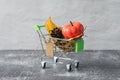 Green small toy shopping cart with birch leaves, cone and pumpkin on a concrete wall background. Price label note with rope for Royalty Free Stock Photo