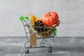 Green small toy shopping cart with birch leaves, cone and pumpkin on a concrete wall background. Price label note with rope for Royalty Free Stock Photo