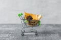 Green small toy shopping cart with leaves, cone on a concrete wall background. Autumn Concept. Royalty Free Stock Photo