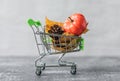 Green small toy shopping cart with leaves, cone and pumpkin on a concrete wall background. Autumn Concept. Royalty Free Stock Photo