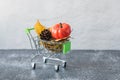 Green small toy shopping cart with leaves, cone and pumpkin on a concrete wall background. Autumn Concept. Royalty Free Stock Photo