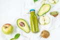 Green smoothie in bottl with avocado, apple and kiwi on white wooden background