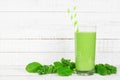 Green smoothie with kale and spinach in a glass on a white wood background