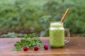 Green smoothie of parsley, avocado, honey and banana in a glass mug on a wooden table in a garden cafe, close-up