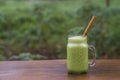 Green smoothie of parsley, avocado, honey and banana in a glass mug on a wooden table in a garden cafe, close-up