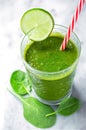 Green smoothie with a slice of lime and red striped drinking straw on a marbled surface