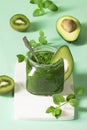 Green smoothie - spinach, kiwi, avocado puree in a glass jar with a spoon, decorated with an avocado slice on a light green Royalty Free Stock Photo