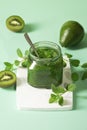 Green smoothie - spinach, kiwi, avocado puree in a glass jar with a spoon on a light green background, fruits are next to it. Royalty Free Stock Photo