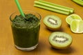 Green smoothie and straw in glass. Kiwi and lime slices, celery stalks on table