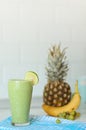 Green smothie in glass with Lemon on top on blured background with ananas banana and grape copy space on top