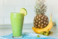 Green smothie in glass with Lemon on top,on blured background with ananas,banana and grape