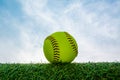 A green softball on the grass with a blue sky in the background