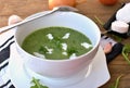 Green soup from arugula and garlic with goat cheese in white bowl with spoon on wooden background