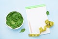 Green spinach leaves, notebook and tape measure on blue table top view. Diet and healthy food concept.