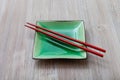 Green square saucer with red chopsticks on gray Royalty Free Stock Photo