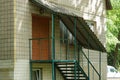 Green staircase with iron steps and metal handrails on an open veranda