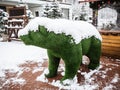 A green statue of a bear made of artificial grass stands strewn with snow on the street