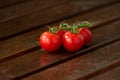 Green stem with four small fresh cherry tomatoes covered in water droplets on brown wood planks in daylight shallow depth of field Royalty Free Stock Photo