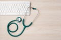 Green stethoscope with computer keyboard on wooden doctor desk background