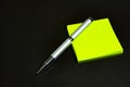 Green stickers and a silver ballpoint pen lie on a black matte surface. Stationery on a black table Royalty Free Stock Photo