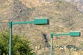 Green street lamps with bird spikes on top with moutainous background and visible tree in afternoon sun Royalty Free Stock Photo