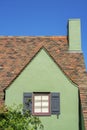 Green stucco house faÃÂ§ade with decorative shutters and dark accent paint with visible chimney and brown roofs tiles and