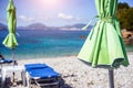 Green sunbed umbrella on white stoe beach by clear turquoise blue waters of Mediterranean sea on sunny hot summer day