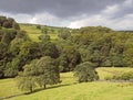 Green sunlit landscape with hillside fields along a tree covered valley with grey clouds in the elphin valley between cragg vale