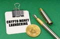 On a green surface, a bitcoin coin, a pen and a sheet of paper with the inscription - Crypto money laundering