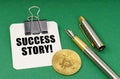 On a green surface, a bitcoin coin, a pen and a sheet of paper with the inscription - Success Story