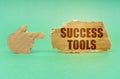 On a green surface, a cardboard hand points to a sign with the inscription - Success Tools