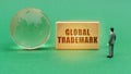 On the green surface is a globe and a figurine of a man who looks at a sign with the inscription - Global Trademark