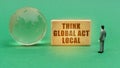 On the green surface is a globe and a figurine of a man who looks at a sign with the inscription -Think global act local Royalty Free Stock Photo